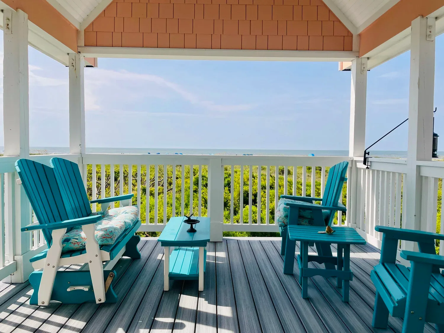 Covered oceanfront porch with turquoise furniture on a coastal home built by Hale Development, overlooking the beach